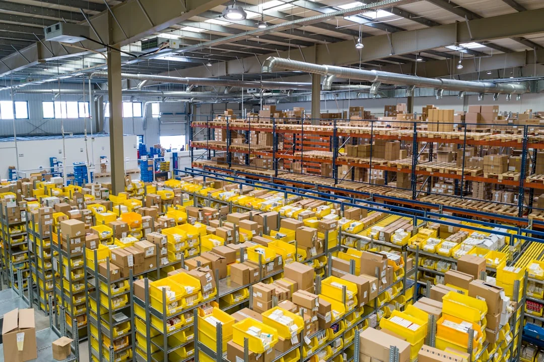A warehouse floor from above: rows of shelving holding picking bins and cartons, with pallet racking behind